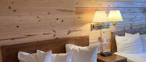 A hotel room with a wooden headboard, a bed with white bedding, two bedside lamps, and a brown textured rug.
