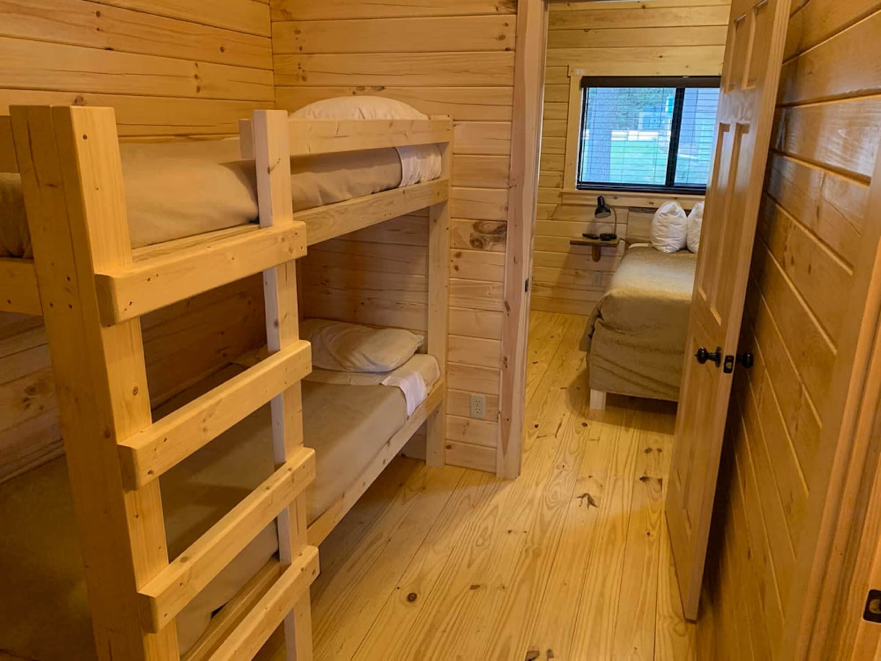 En træhytte med køjesenge, et lille skrivebord med stol og et vindue med skodder.