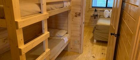 A wooden cabin with bunk beds, a small desk with a chair, and a window with blinds.
