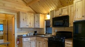 A wooden cabin interior with a kitchen area featuring wooden cabinets, a stove, a microwave, and a refrigerator. - Waterfront Inn - Mackinaw City (Mackinaw City)