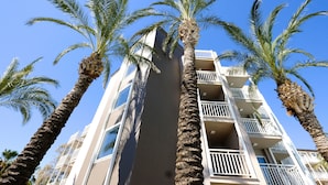 Un hotel de varios pisos con balcones, palmeras y un cielo azul despejado.