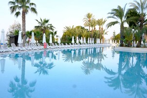 Una piscina con sillas de descanso y sombrillas, rodeada de palmeras.