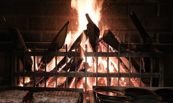 Una parrilla con fuego ardiendo al fondo, rodeada de rejillas metálicas.