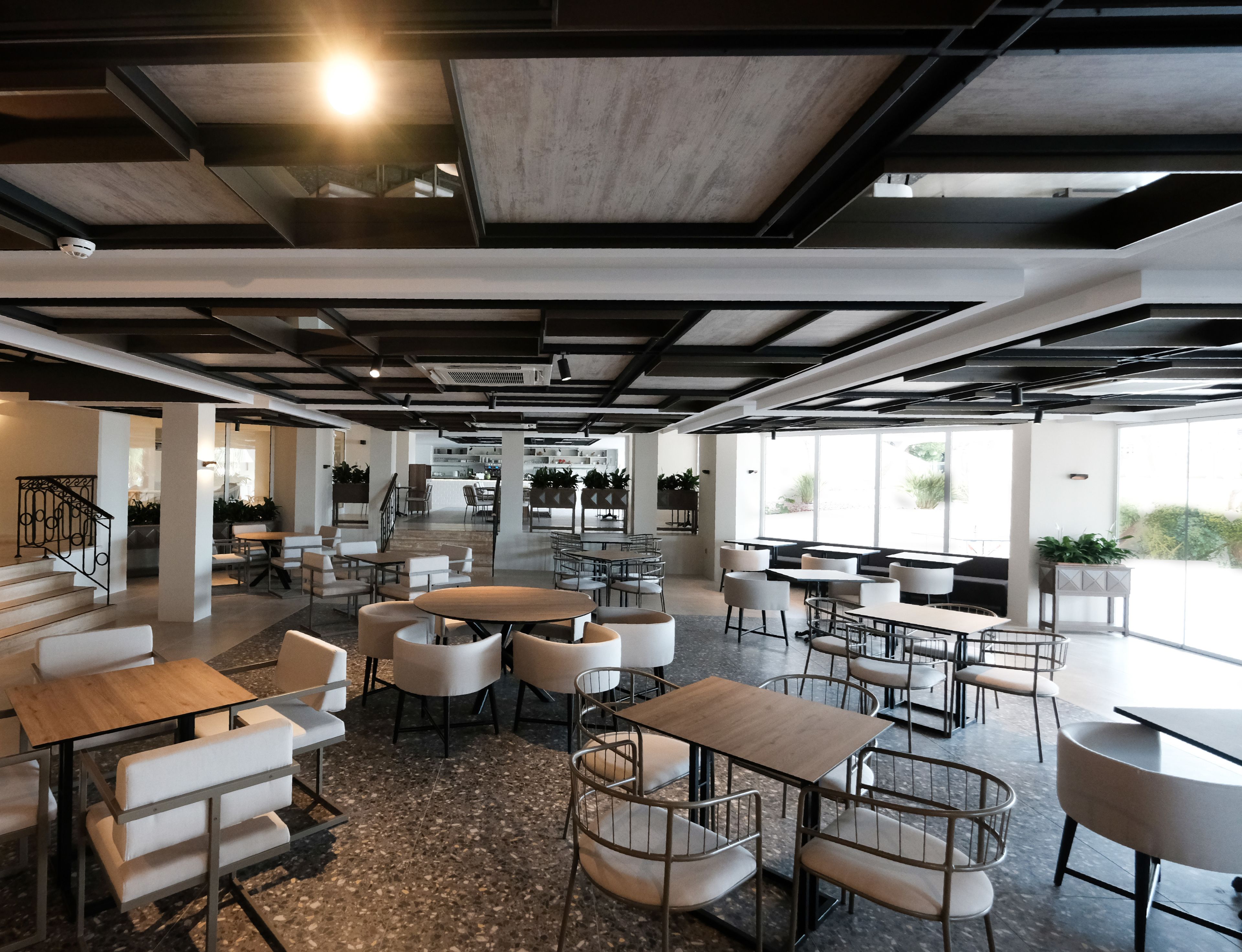 Un café moderne avec un mélange de tables rondes et rectangulaires, certaines dotées de chaises rembourrées blanches et d'autres de structures métalliques.