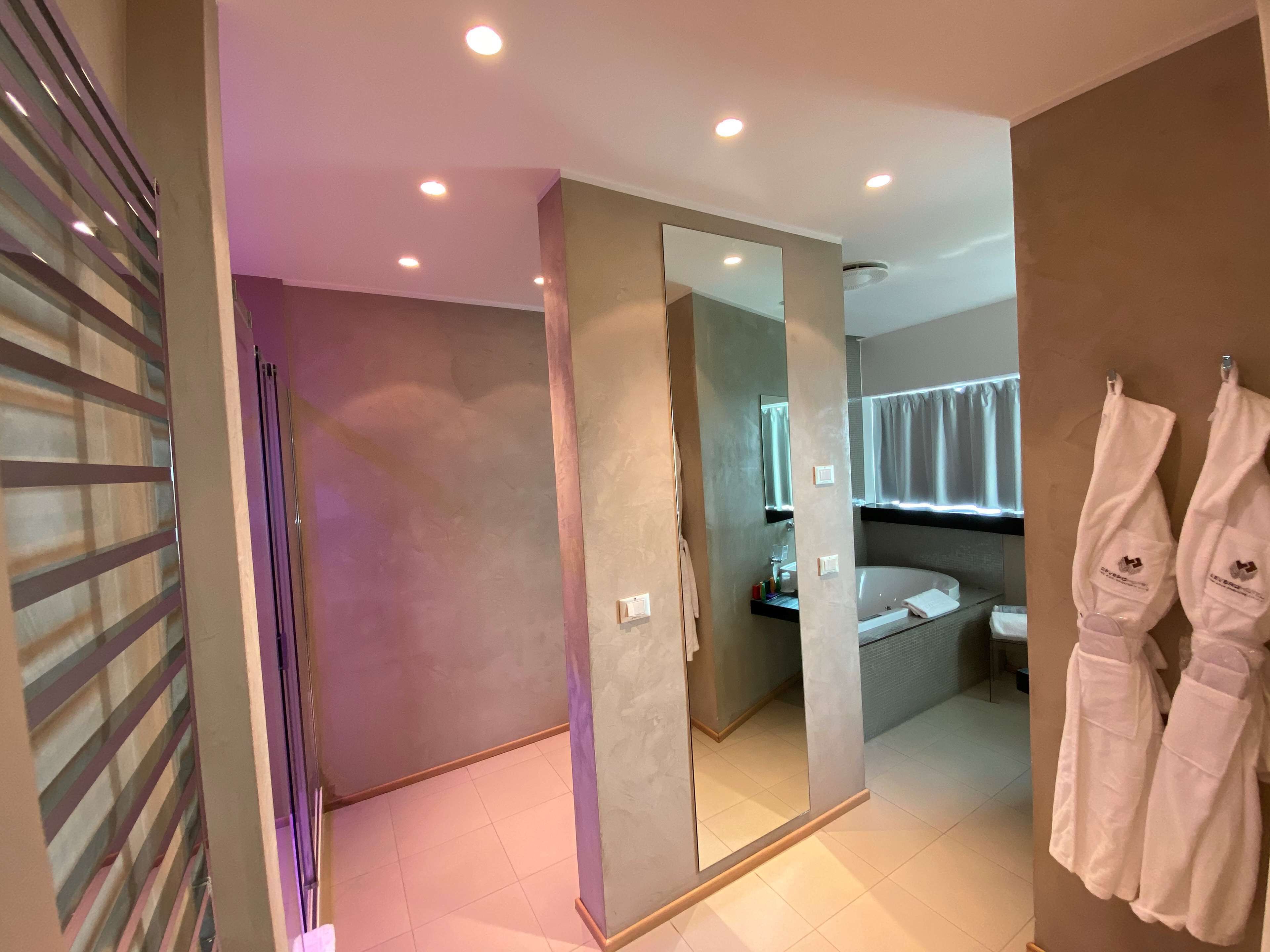 A modern bathroom with a large mirror, a bathtub, and two white robes hanging on the wall.
