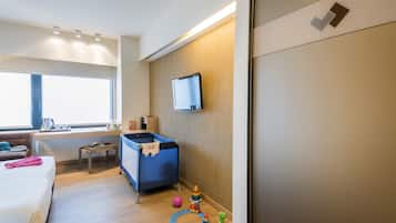 Ein Hotelzimmer mit einem Bett, einem Schreibtisch, einem Fernseher, einem blauen Reisebett und Spielzeug auf dem Boden.