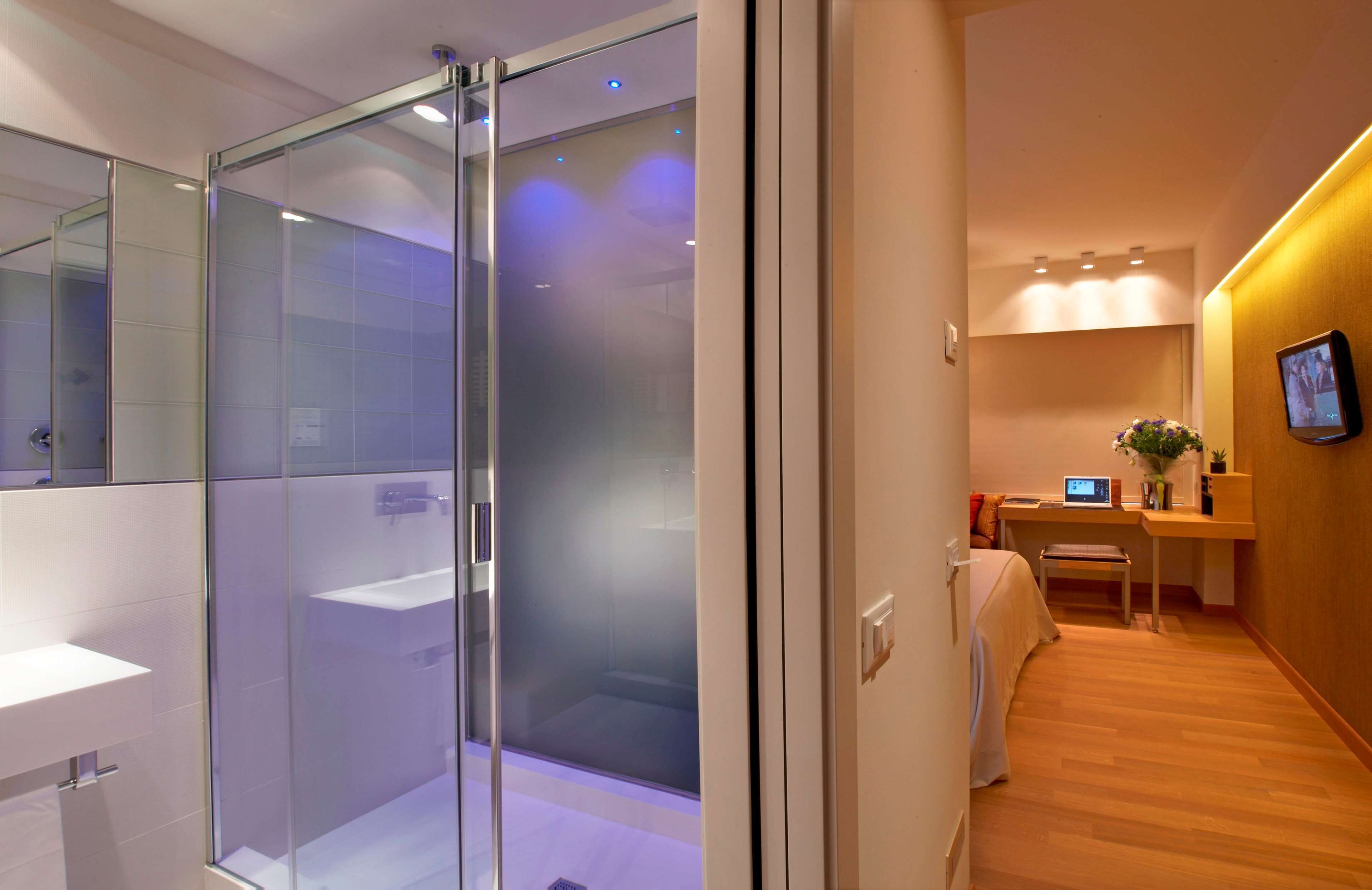 A modern bathroom with a glass shower enclosure, a white sink, and a wooden floor.