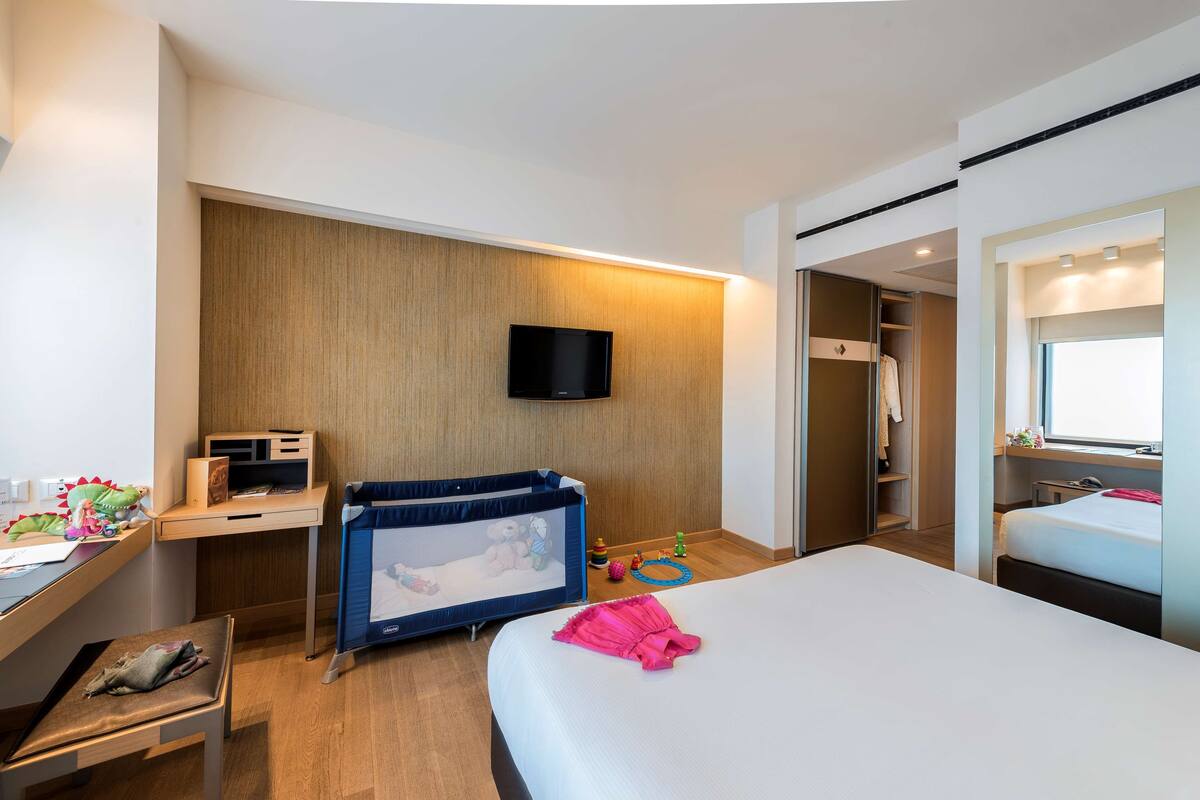 Een moderne hotelkamer met een bed, een bureau, een televisie, een kledingkast en een klein ledikantje.