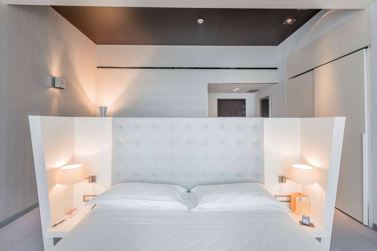 Een moderne hotelkamer met een groot bed, twee nachtkastjes en wandlampen.