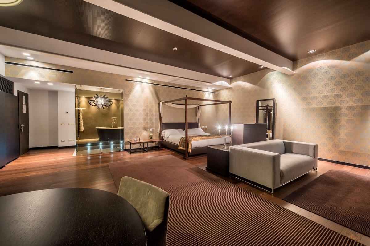 Een moderne hotelkamer met een hemelbed, een bank, een eettafel en een spiegel.