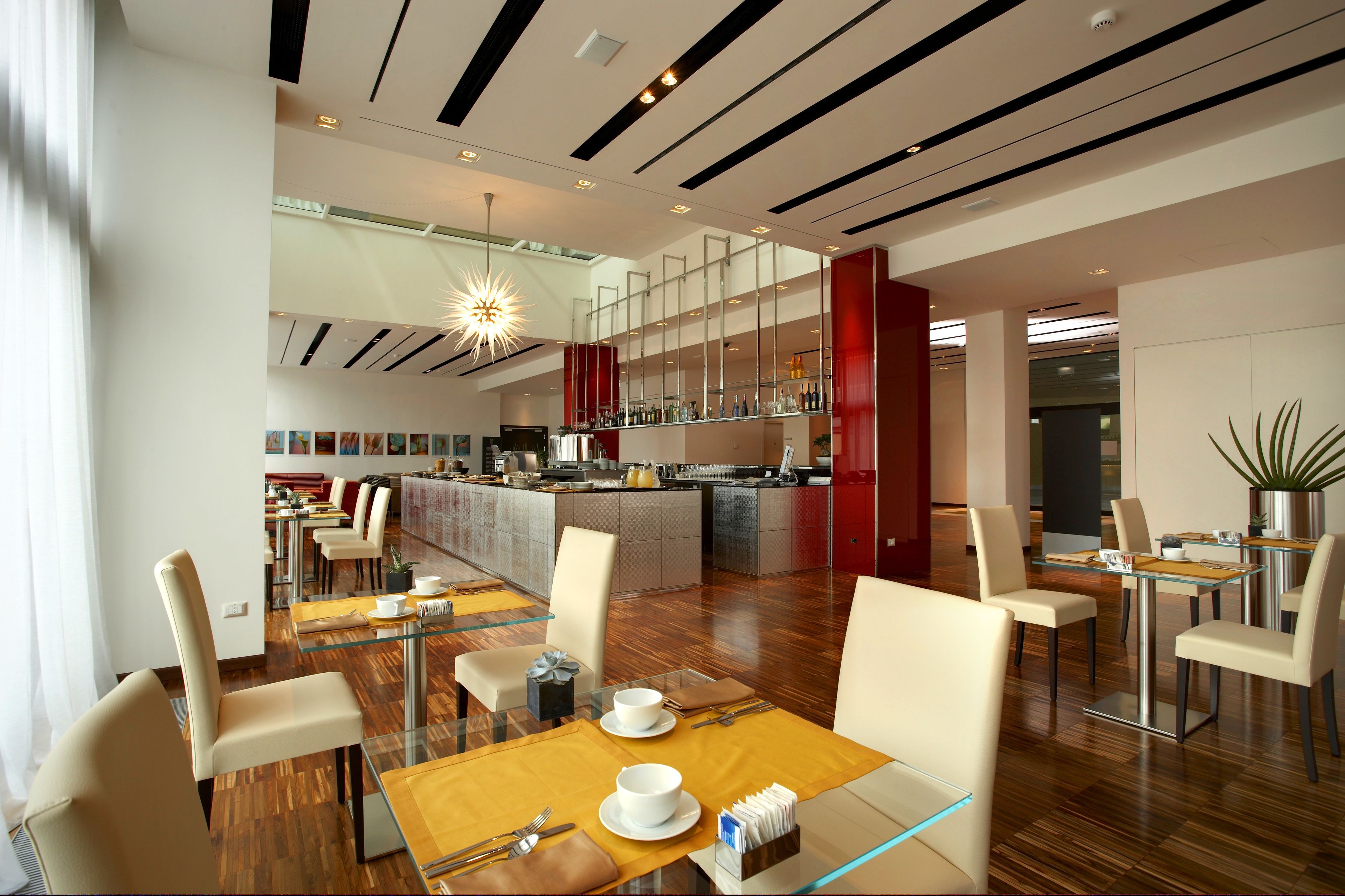 A modern hotel lobby with a central bar area, dining tables, and a large potted plant.