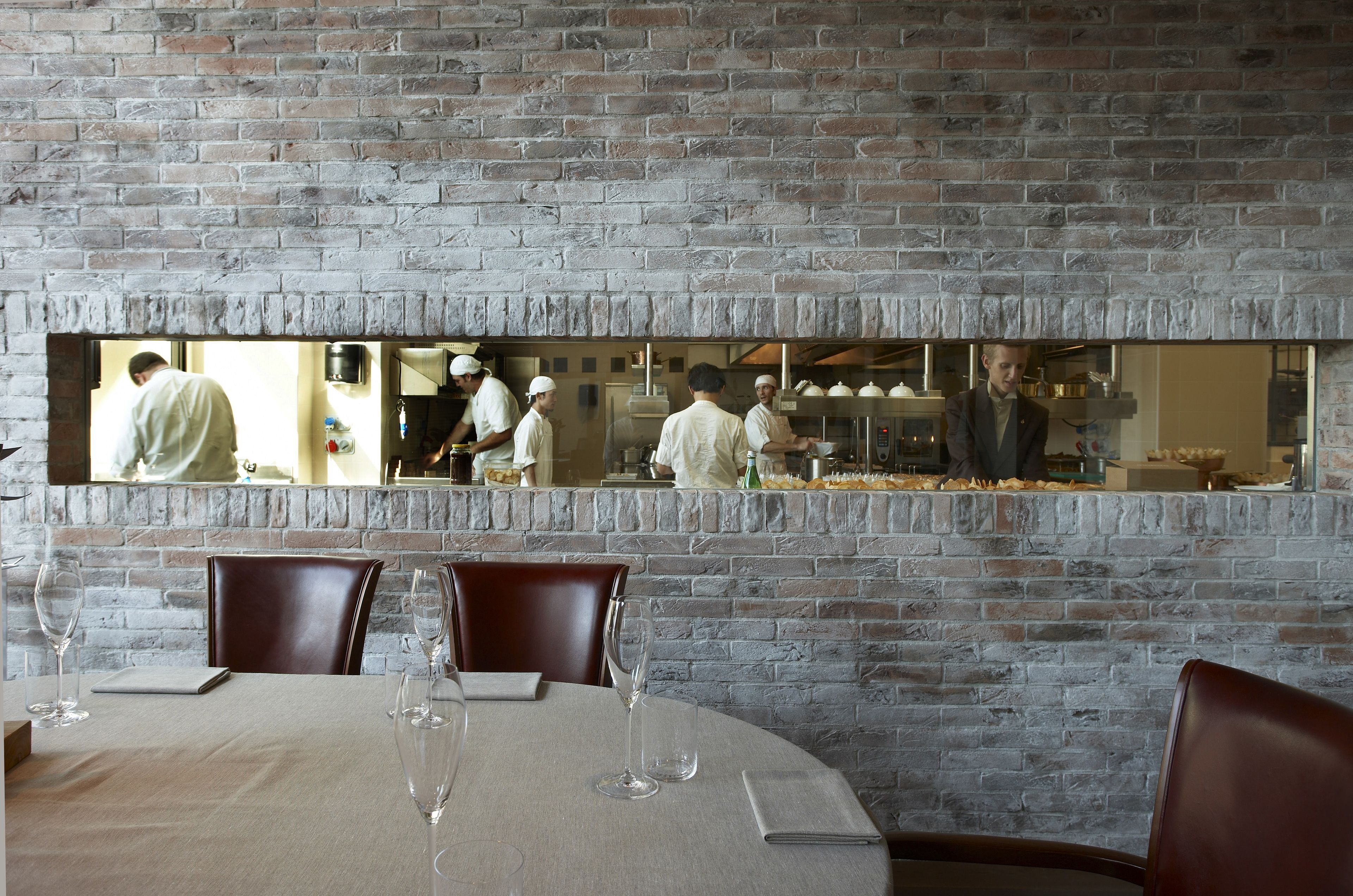 Un restaurant avec un mur en briques et un grand miroir qui reflète l’espace cuisine.