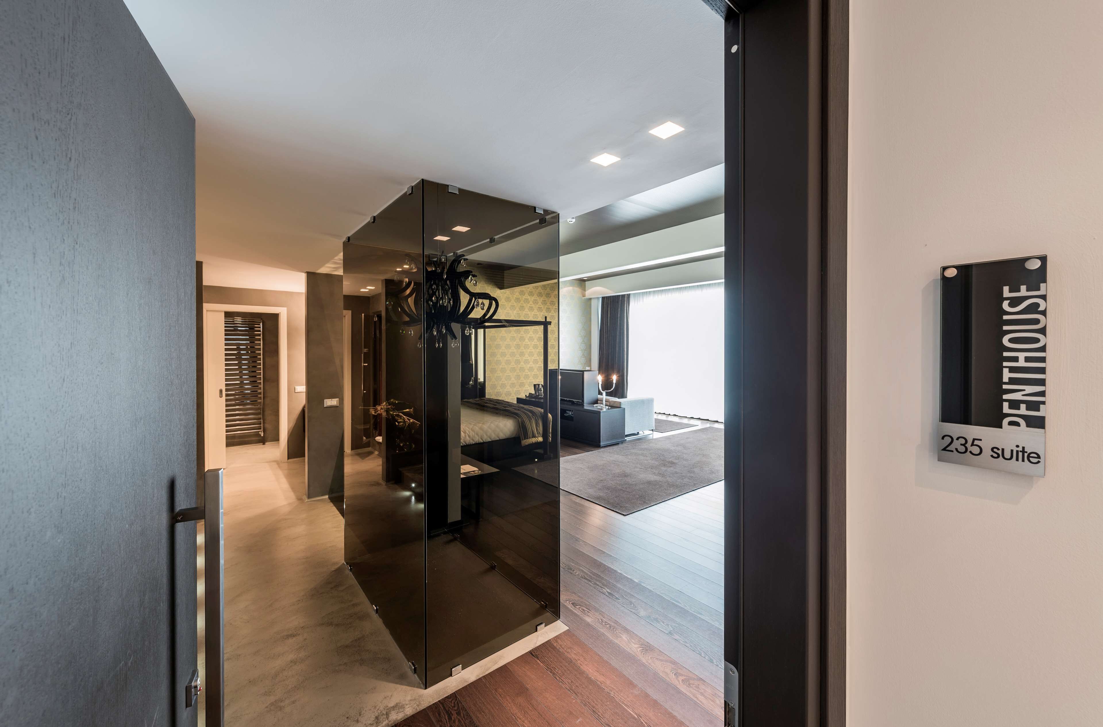 A modern hotel interior with a glass partition, a bed, a desk, and a sign indicating "Penthouse 235 suite".