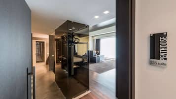 A modern hotel interior with a glass partition, a bed, a desk, and a sign indicating "Penthouse 235 suite".
