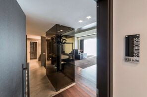 Un intérieur d’hôtel moderne avec une cloison en verre, un lit, un bureau et une pancarte indiquant « Suite Penthouse 235 ».