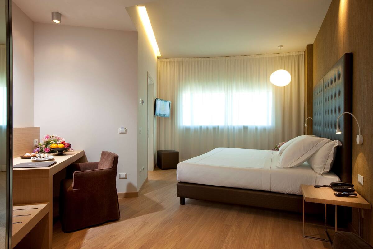 Een hotelkamer met een bed, nachtkastje, bureau, stoel en een televisie aan de muur.