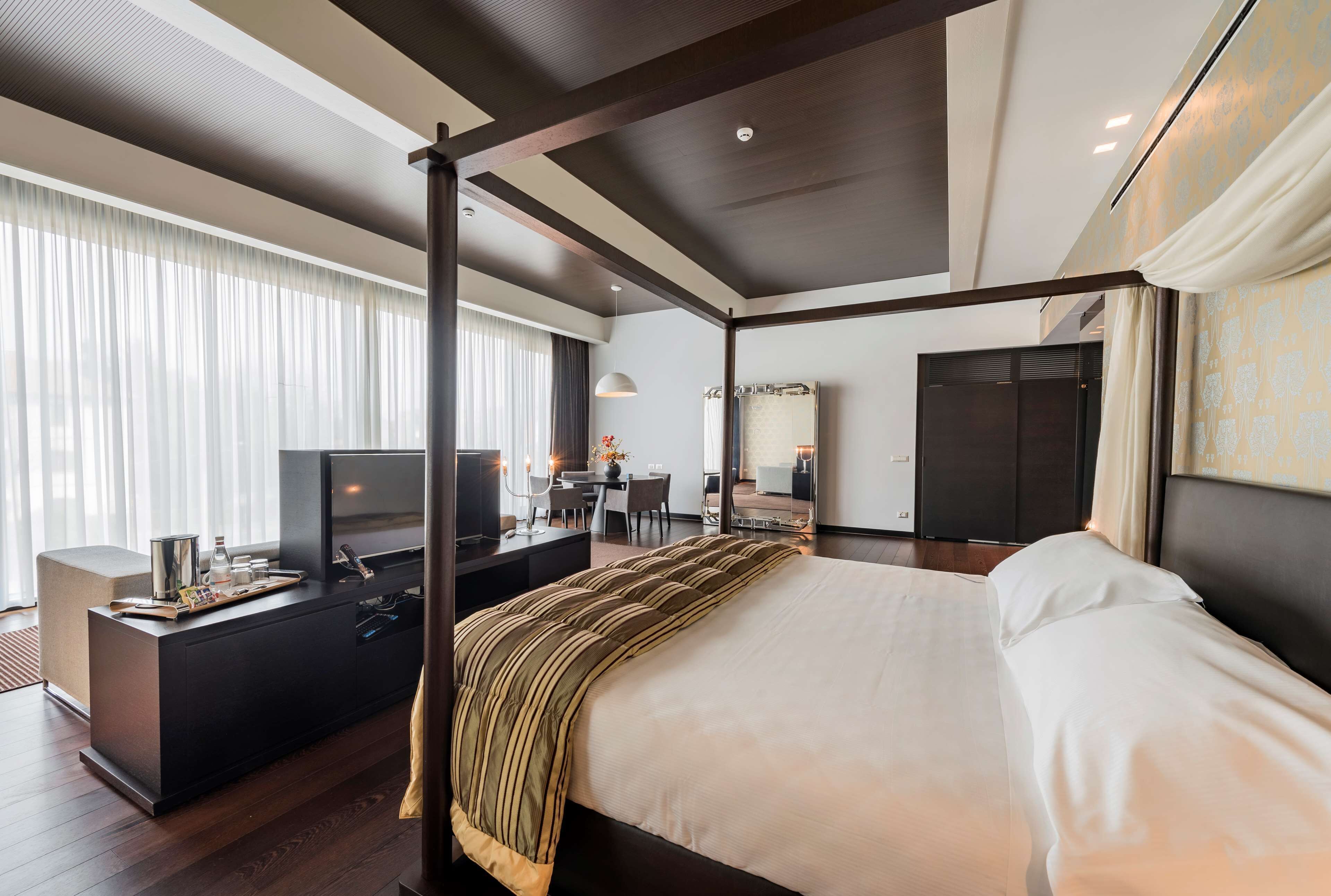 Una habitación de hotel moderna con una cama con dosel, un escritorio con televisor y un comedor.
