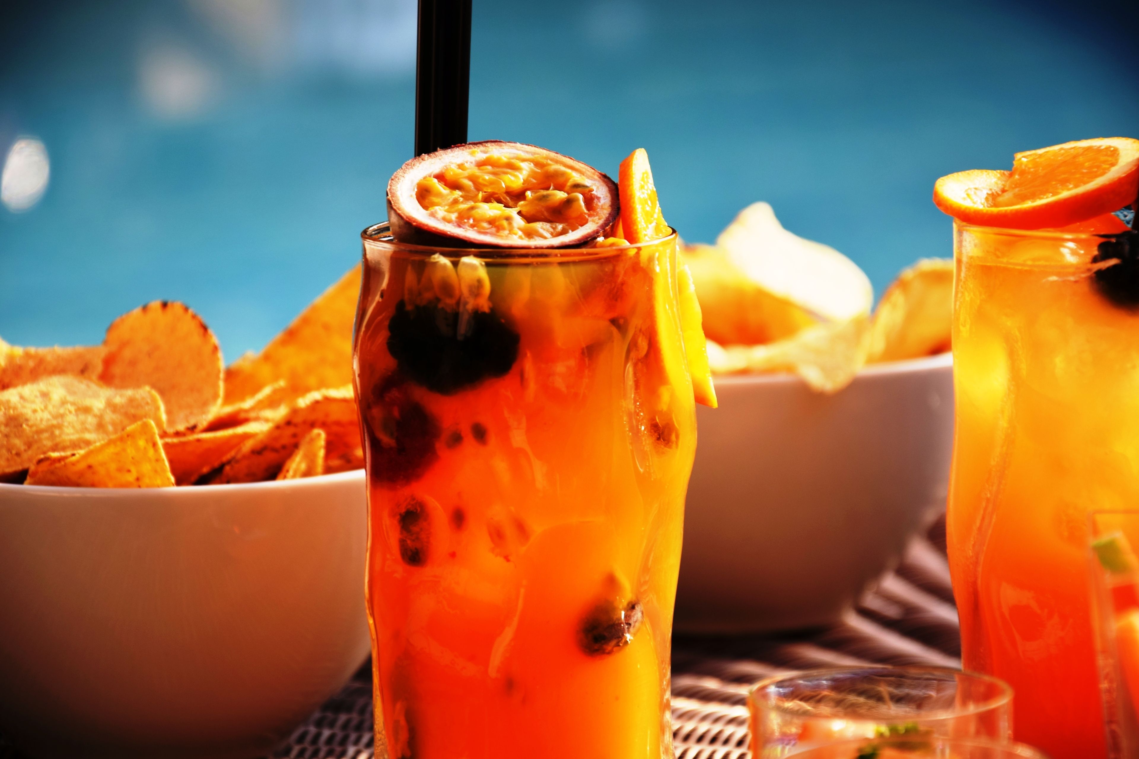 Ein Glas orangefarbenes Getränk mit Passionsfruchtstückchen und Orangenscheibe, dazu eine Schale Tortilla-Chips.
