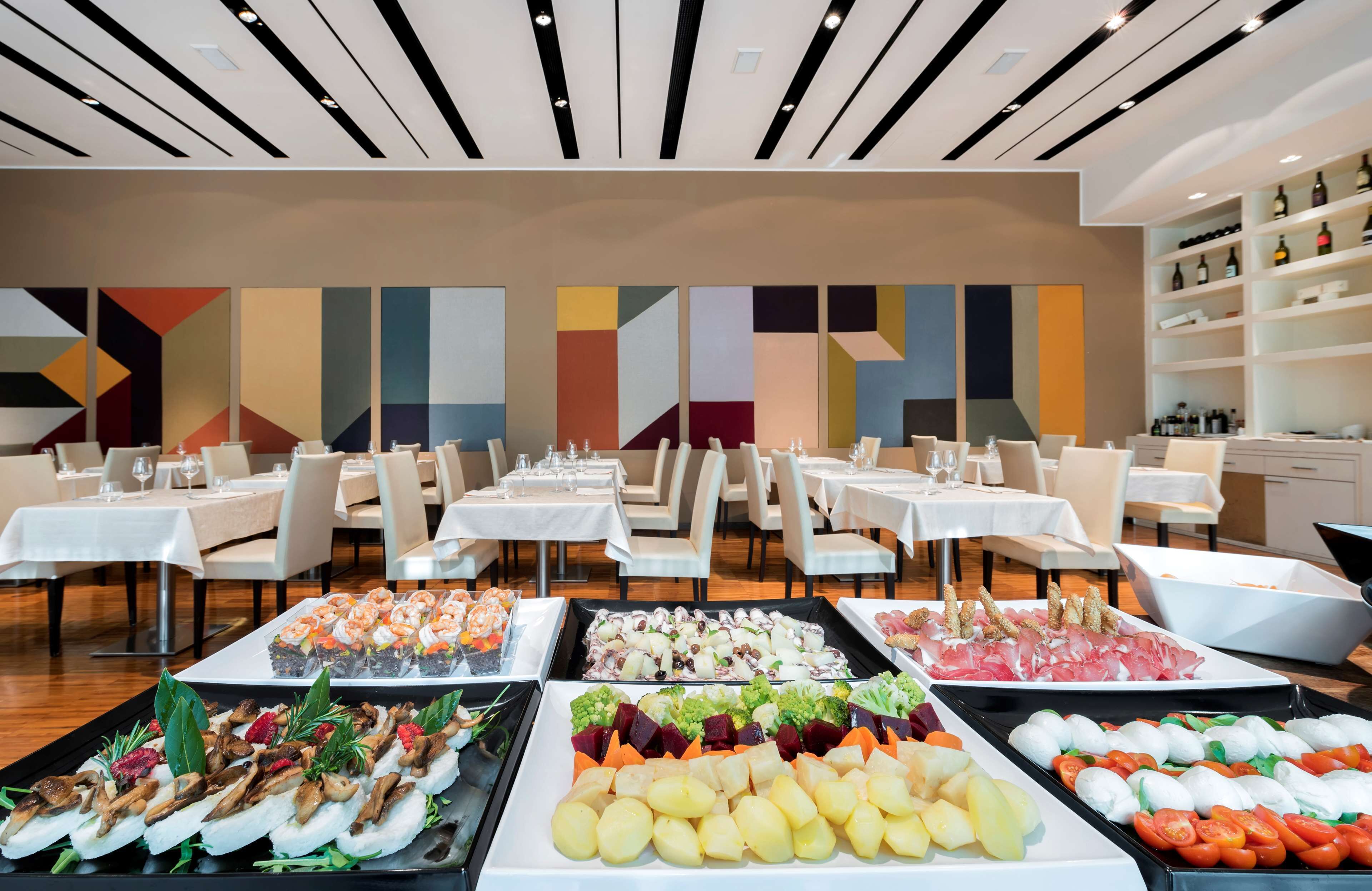 A hotel dining area with multiple tables, a variety of food platters, and a modern geometric wall design.