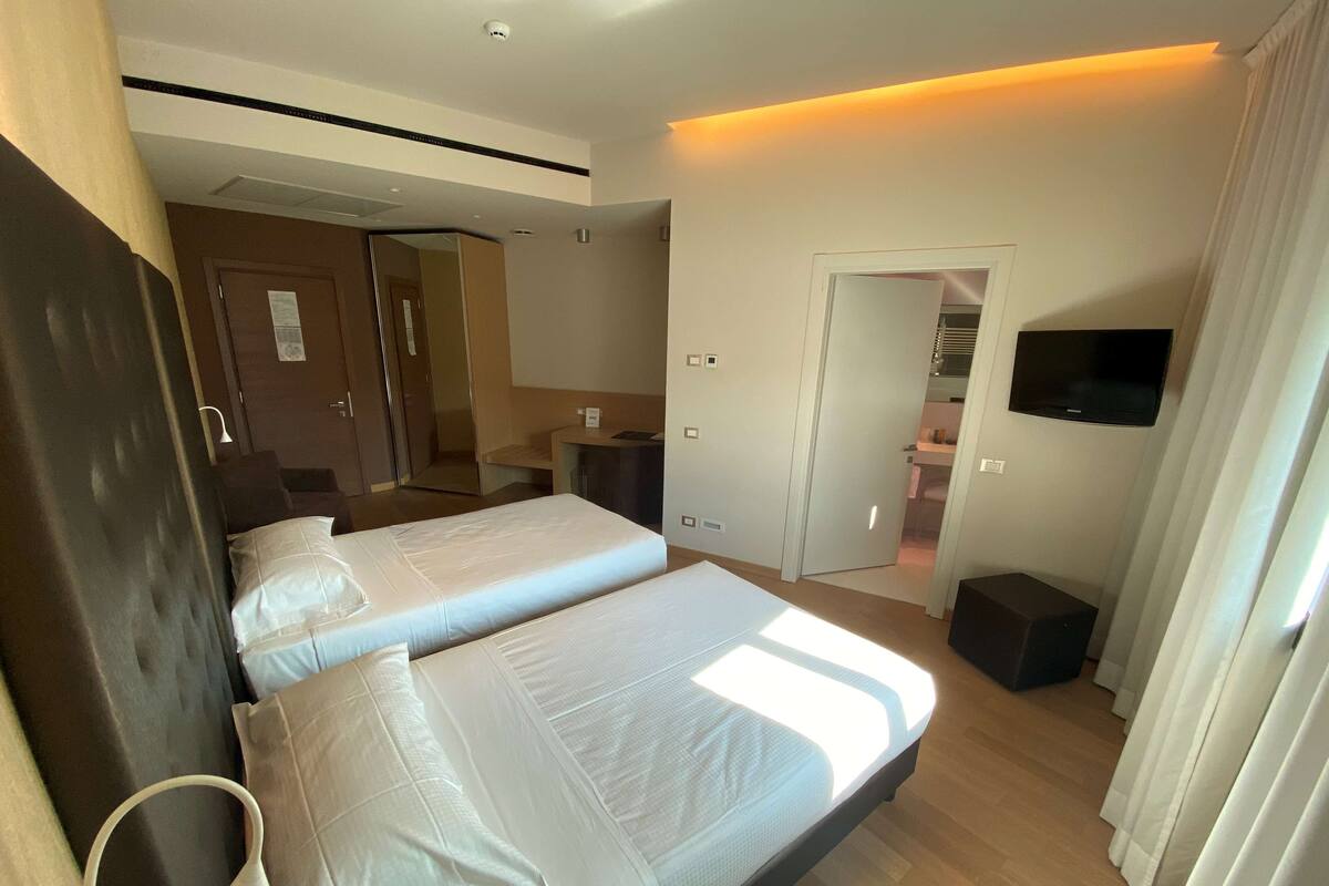 Een hotelkamer met twee bedden, een bureau, een televisie en een badkamer zichtbaar door een geopende deur.