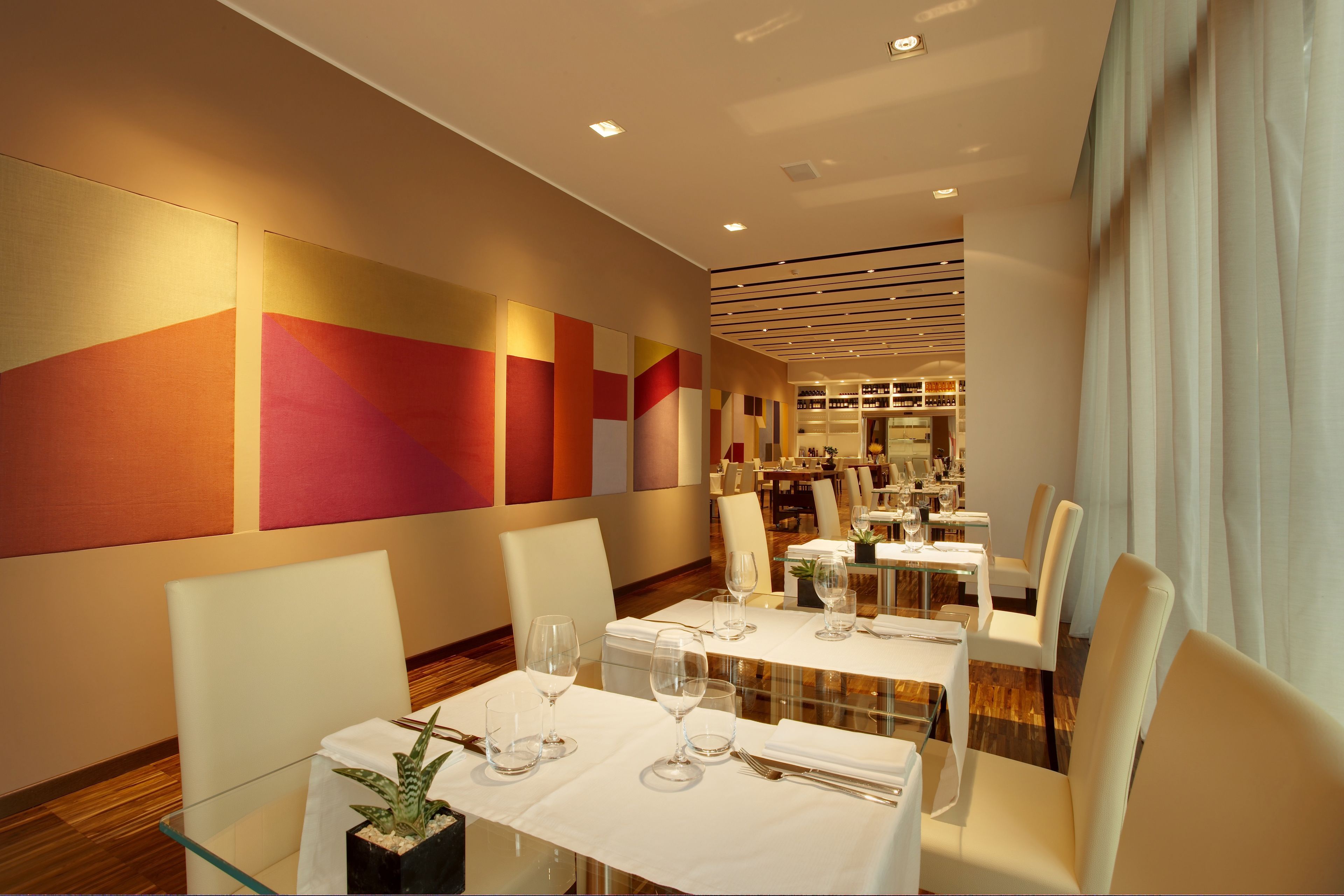 Un espace de restauration moderne avec des tables pour deux personnes, dotées de plateaux en verre et recouvertes de nappes blanches.