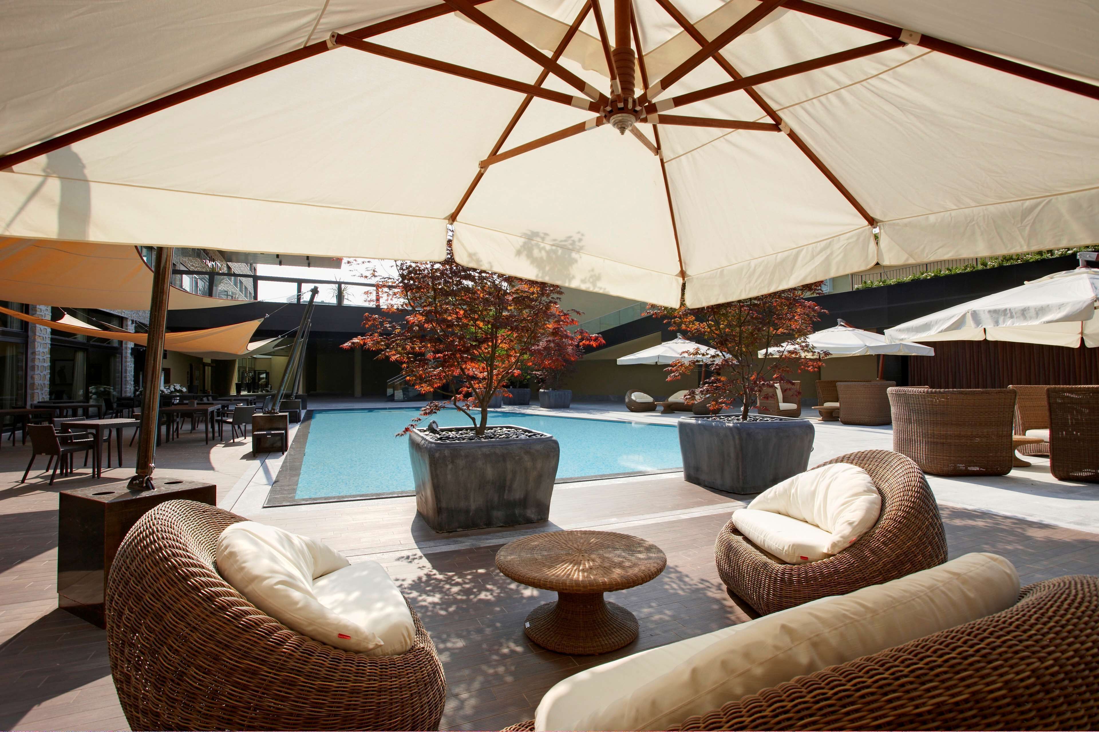 A poolside area with wicker furniture, umbrellas, and potted plants.