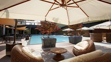 A poolside area with wicker furniture, umbrellas, and potted plants.