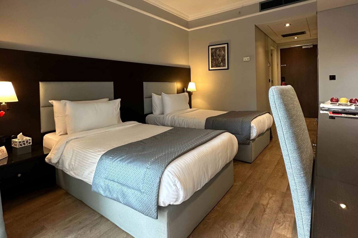 Habitación de hotel con dos camas, cada una con cabecero, mesitas de noche y lámparas.
