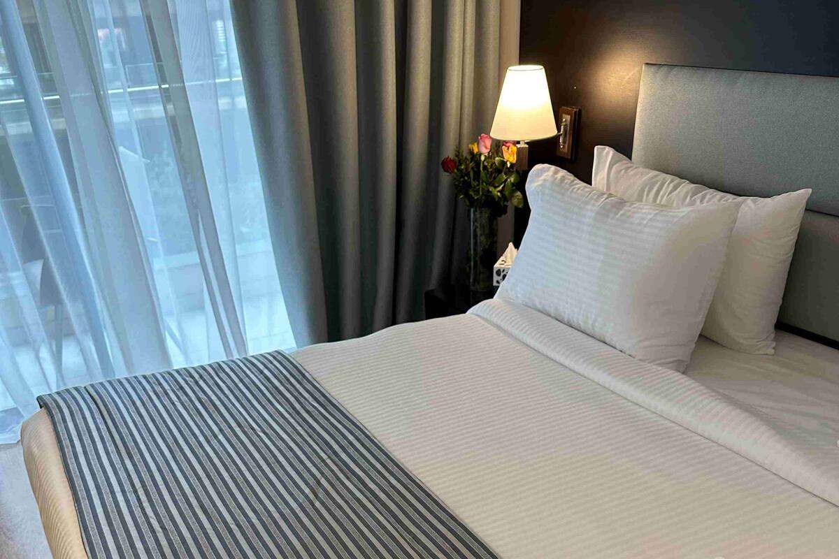 Una habitación de hotel con una cama, una mesita de noche con lámpara y una ventana con cortinas.