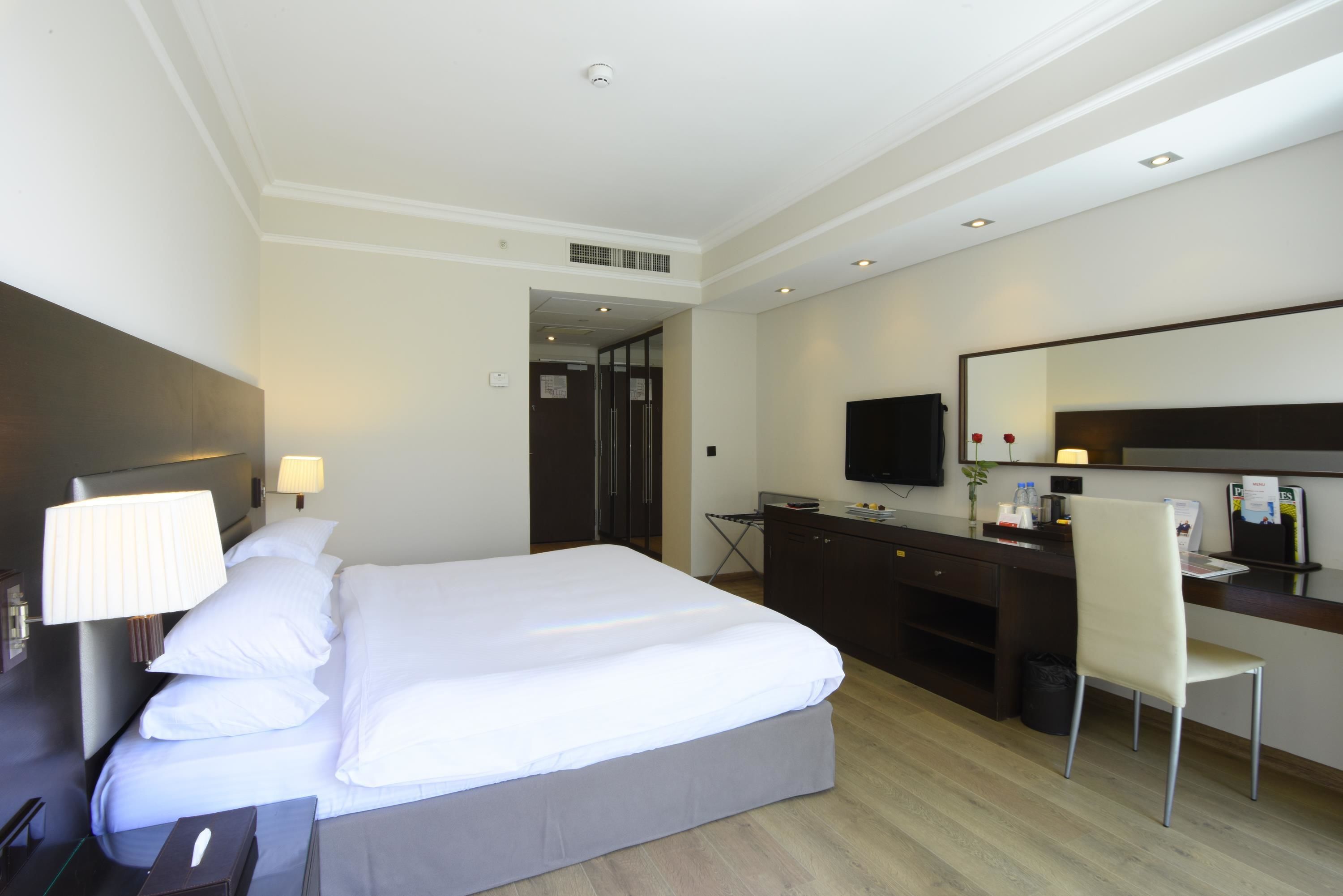 A hotel room with a large bed, a desk, a chair, a TV, and a mirror.