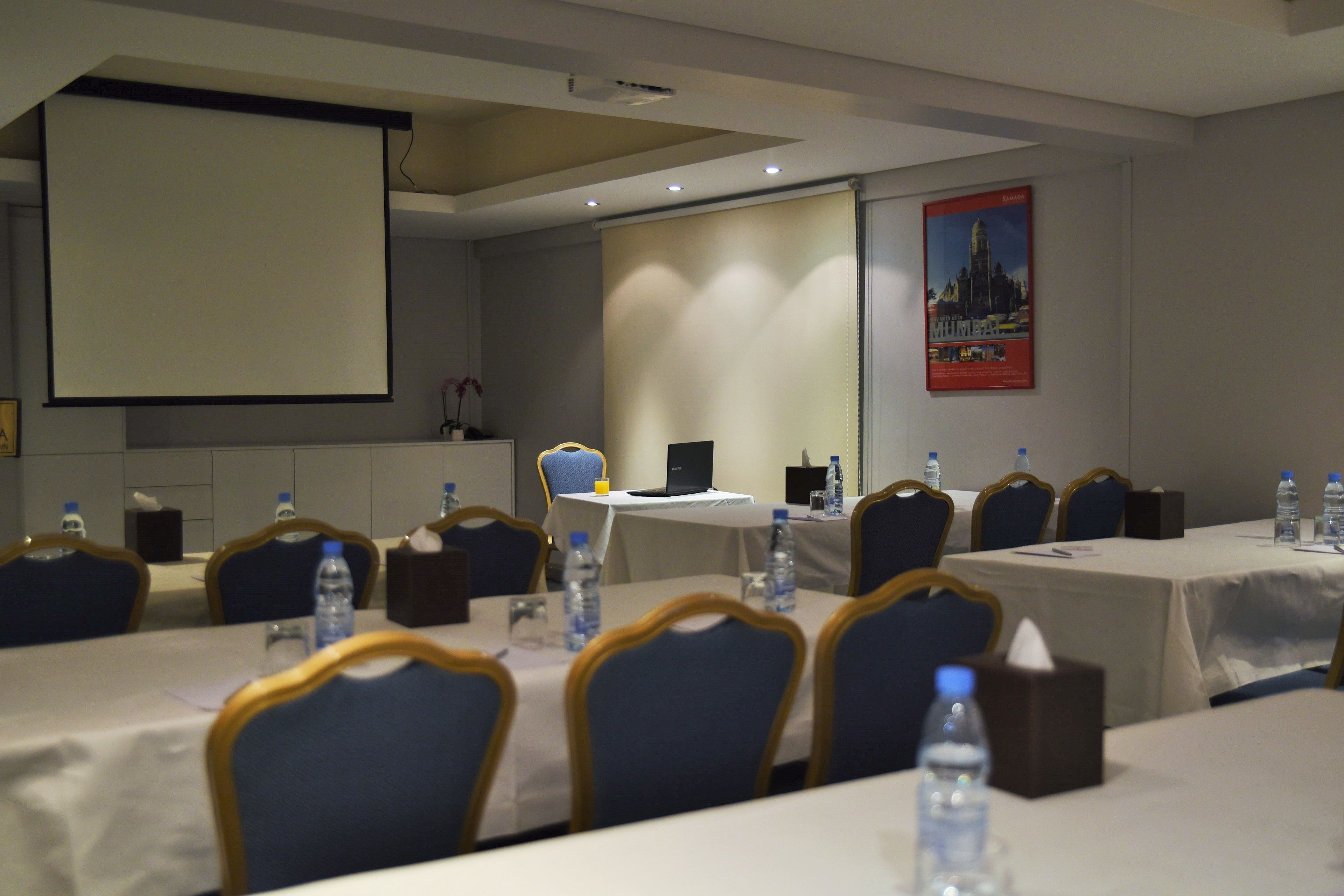 Un salón de conferencias con mesas, sillas, botellas de agua y una pantalla de proyector.