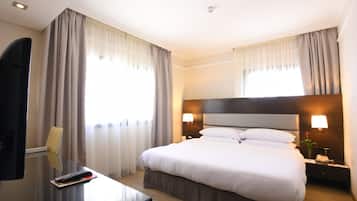 A hotel room with a large bed, bedside lamps, a desk with a remote control, and curtains.