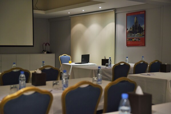 A conference room with tables, chairs, laptops, water bottles, and a projector screen. - Ramada by Wyndham Downtown Beirut (Beirut)