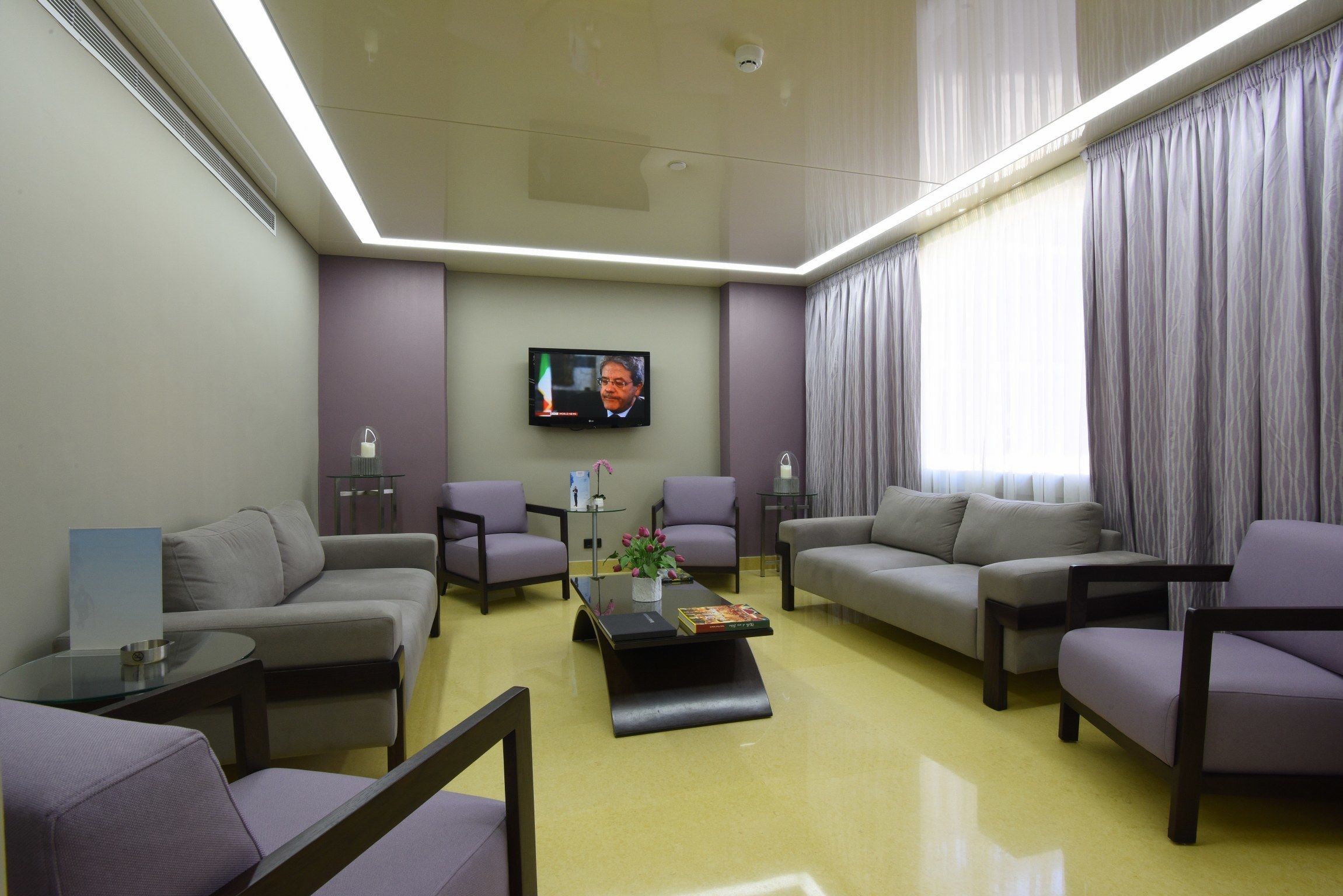 Una sala de estar moderna con un televisor de pantalla plana montado en la pared, dos sofás, una mesa de centro y una mesita auxiliar con un jarrón de flores.