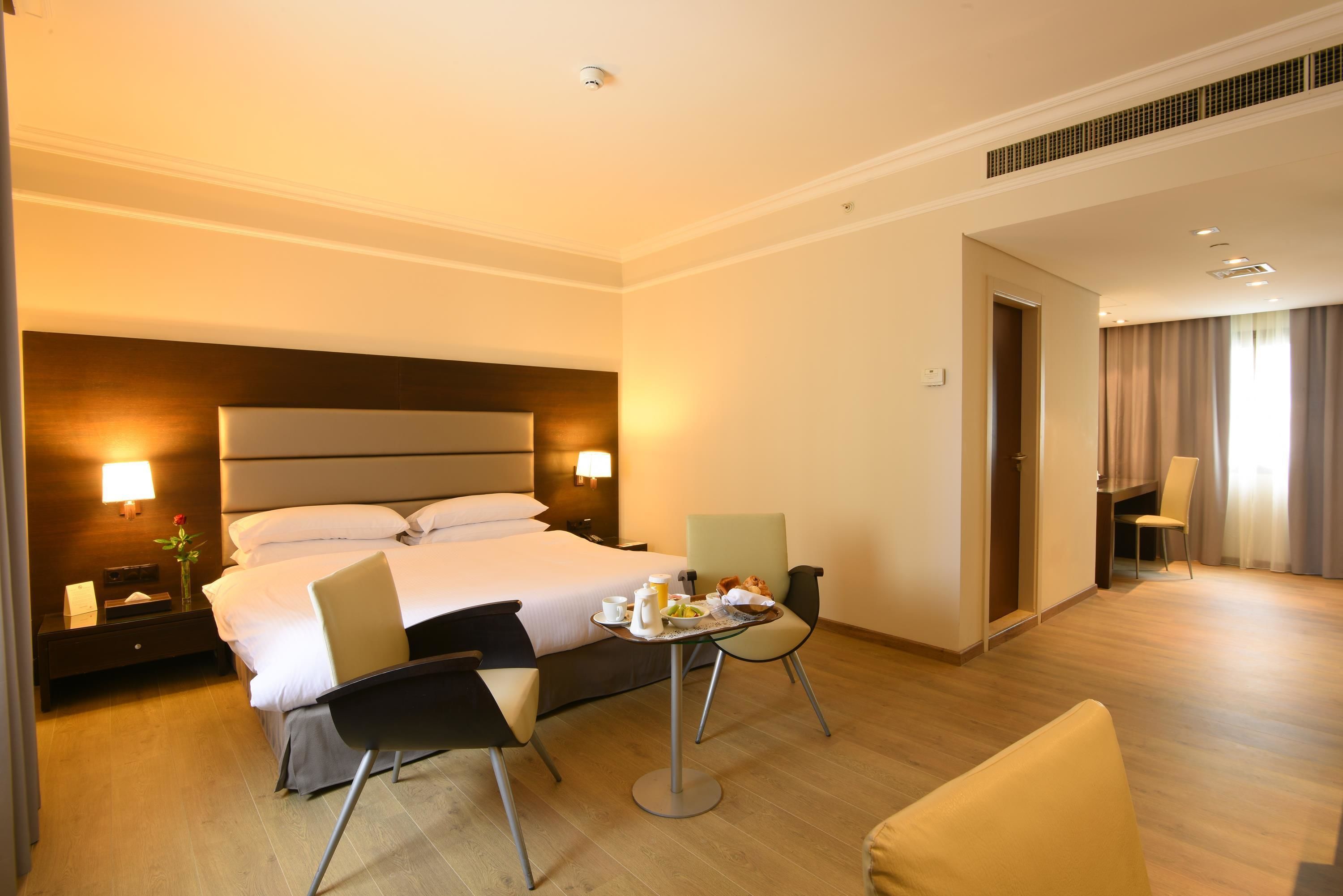 Habitación de hotel con cama, mesitas de noche, una pequeña mesa con alimentos para el desayuno, una silla y un escritorio.