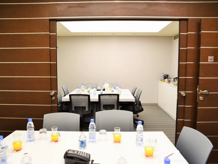 Un salón de conferencias con una mesa dispuesta para una reunión, equipado con botellas de agua, vasos y un teléfono.
