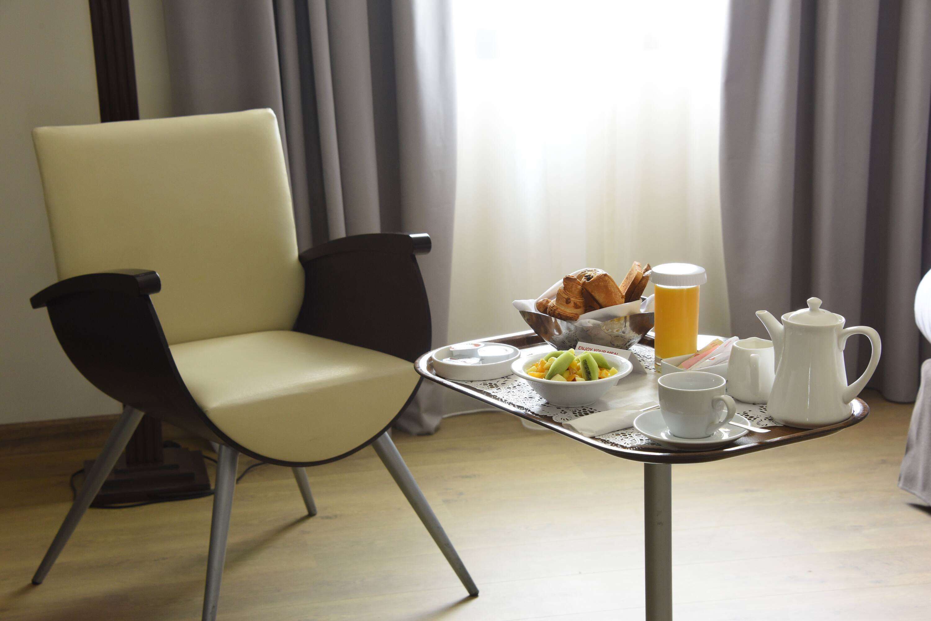 A breakfast setup with a chair, table, and breakfast items including croissants, fruit, and a coffee pot.