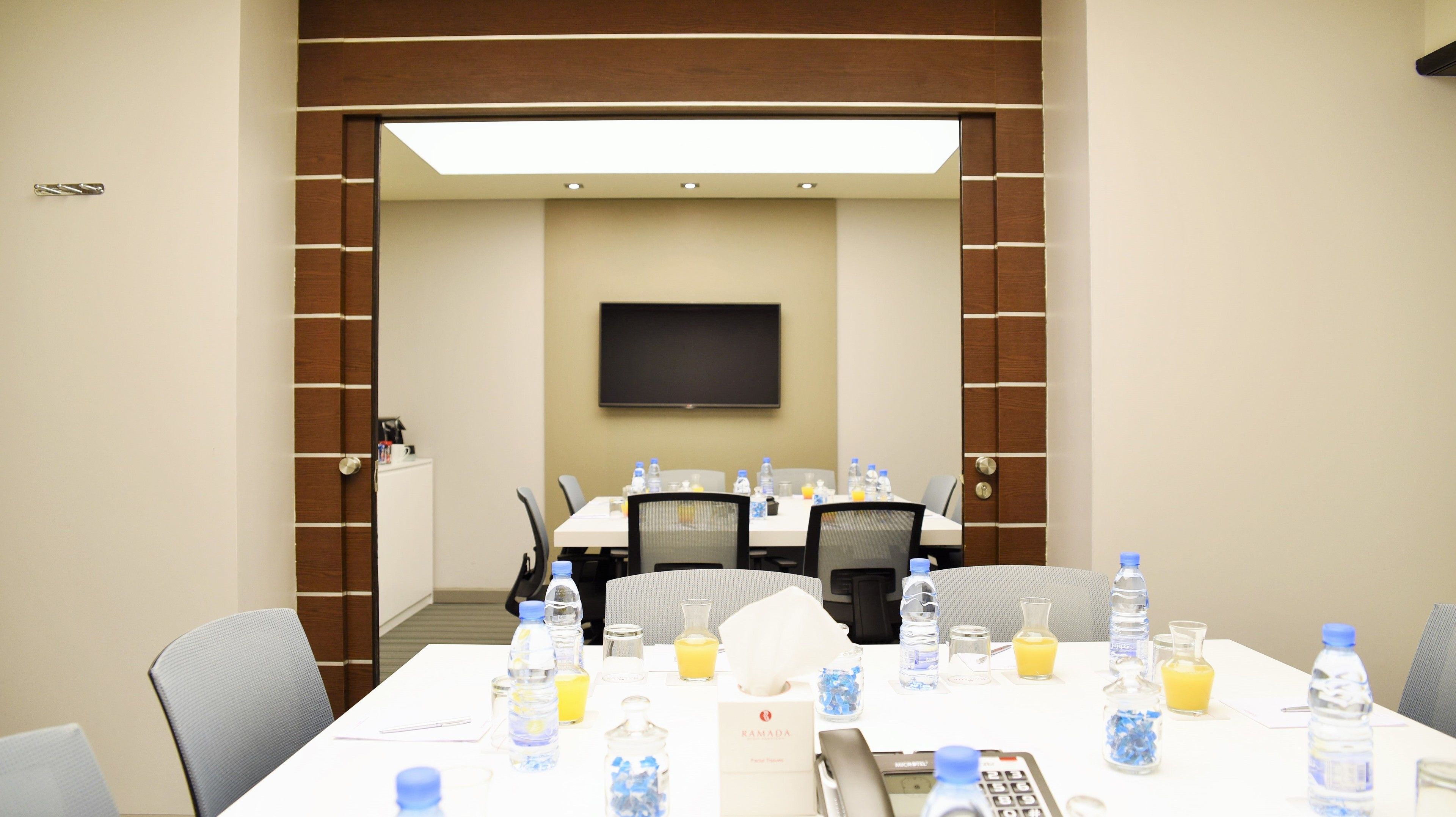 A conference room with a large table, chairs, water bottles, glasses, and a TV screen.