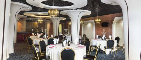 A formal dining area with round tables, black chairs, and chandeliers.