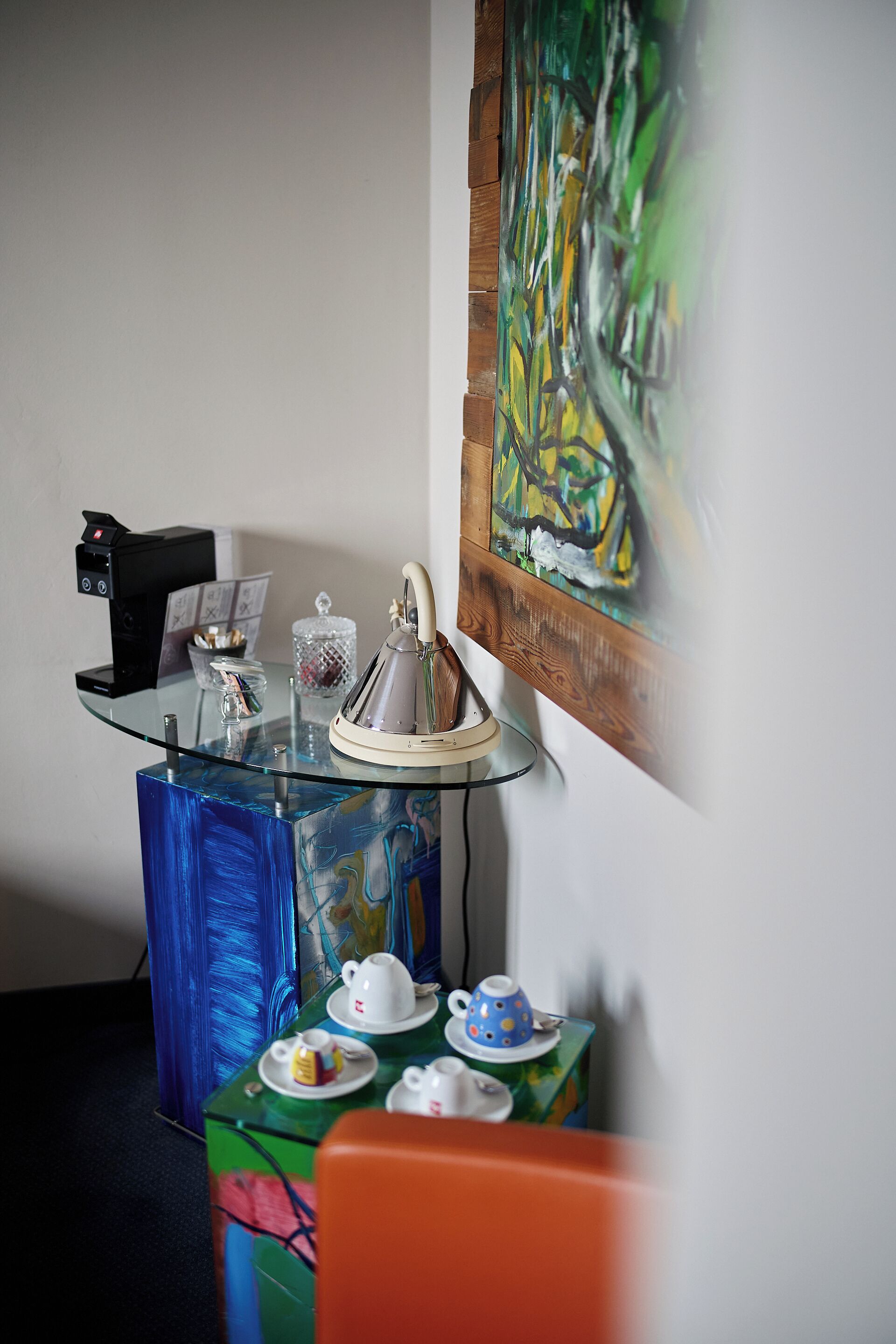 A modern room with a glass coffee table, a painting on the wall, and a coffee machine.