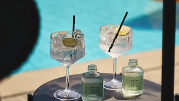 A table with two drinks, each with a lime wedge and straw, and two bottles labeled 'MATCH TONIC WATER' on a poolside setting.