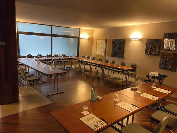 Sala de conferência com mesas compridas, cadeiras e tela de projeção.