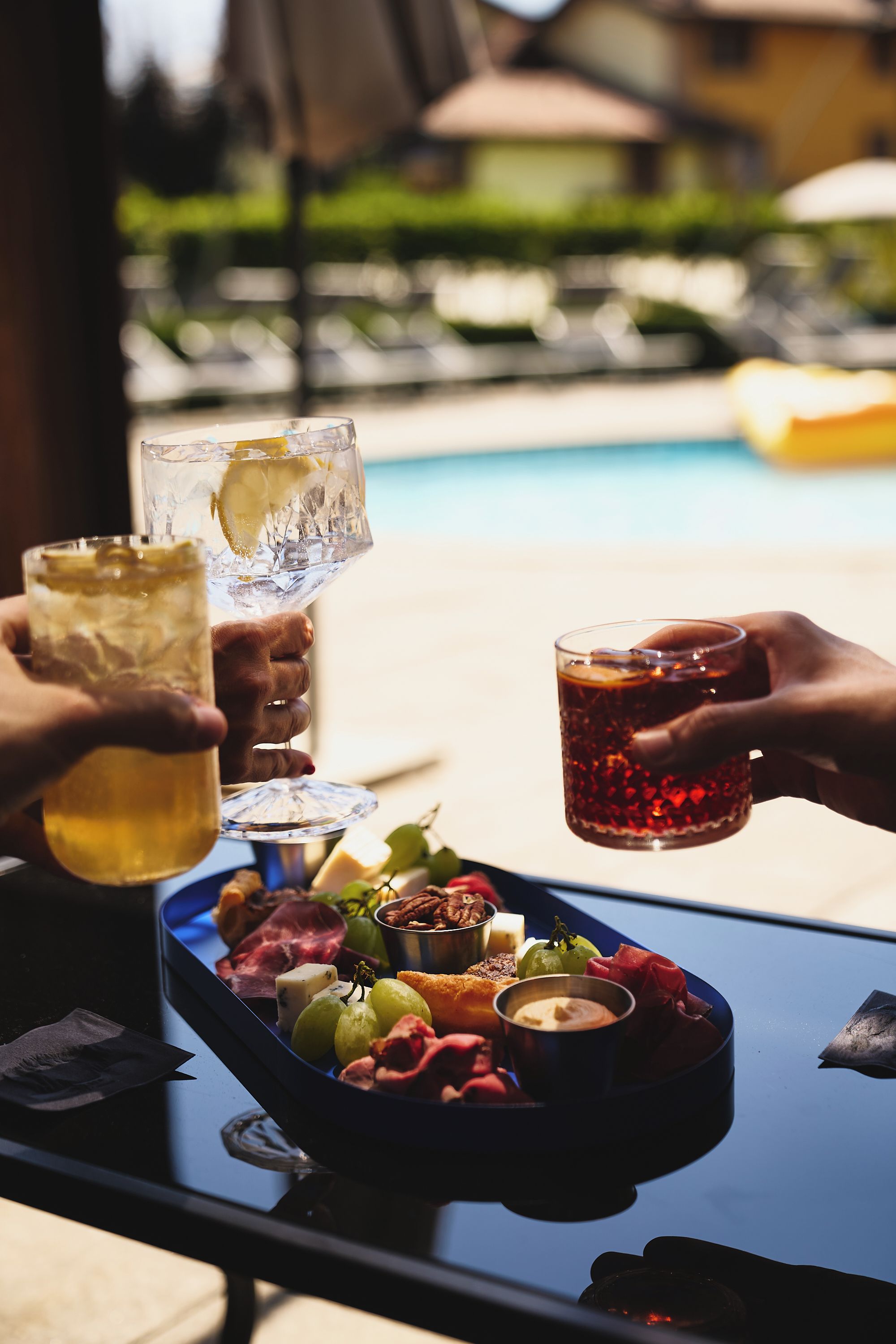 A table with a variety of food items and drinks, including a tray of cheeses, meats, and fruits, and glasses of beverages.