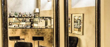 A bar area with two large mirrors, a bar counter with bottles, and two chairs.