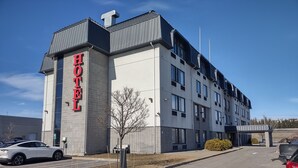 A modern hotel building with a prominent 'HOTEL' sign on the facade, multiple windows, and a parking lot with cars. - Repotel Henri IV Québec (Québec City)