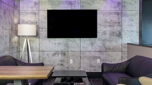 A modern lounge area with a flat-screen TV mounted on a textured wall, a wooden coffee table, a black sofa, and a cream-colored armchair. - Repotel Henri IV Québec (Québec City)