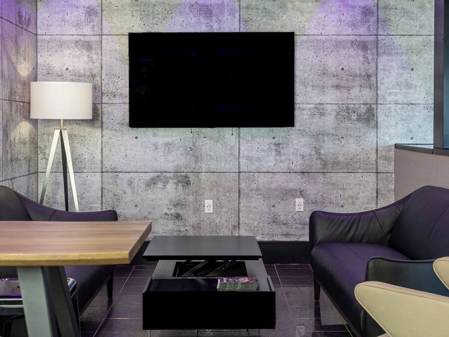 Un salon moderne doté d’un téléviseur à écran plat fixé sur un mur texturé, d’une table basse en bois, d’un canapé noir et d’un fauteuil de couleur crème.