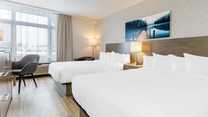 A hotel room with two beds, a desk, a chair, and a large window with curtains. - Repotel Henri IV Québec (Québec City)