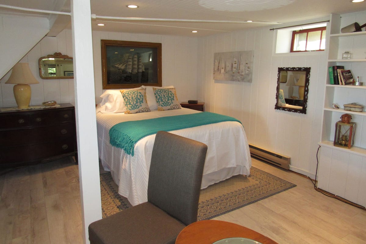 A bedroom with a bed, a chair, a dresser, a mirror, and a shelf with books.