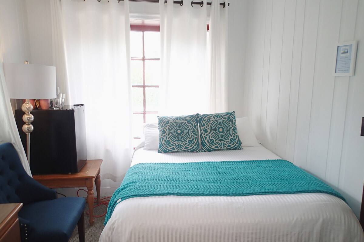 A bedroom with a bed, a desk, a chair, and a window with curtains.